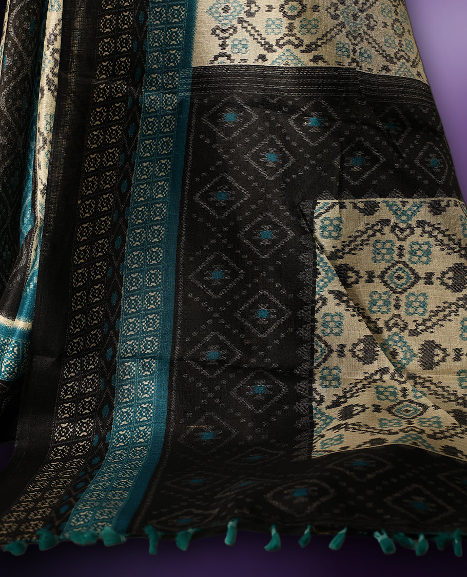 Charming teal, black, and cream printed saree featuring intricate geometric and floral designs, accentuated with a bold black border and tassel finish & paired with a matching blouse.