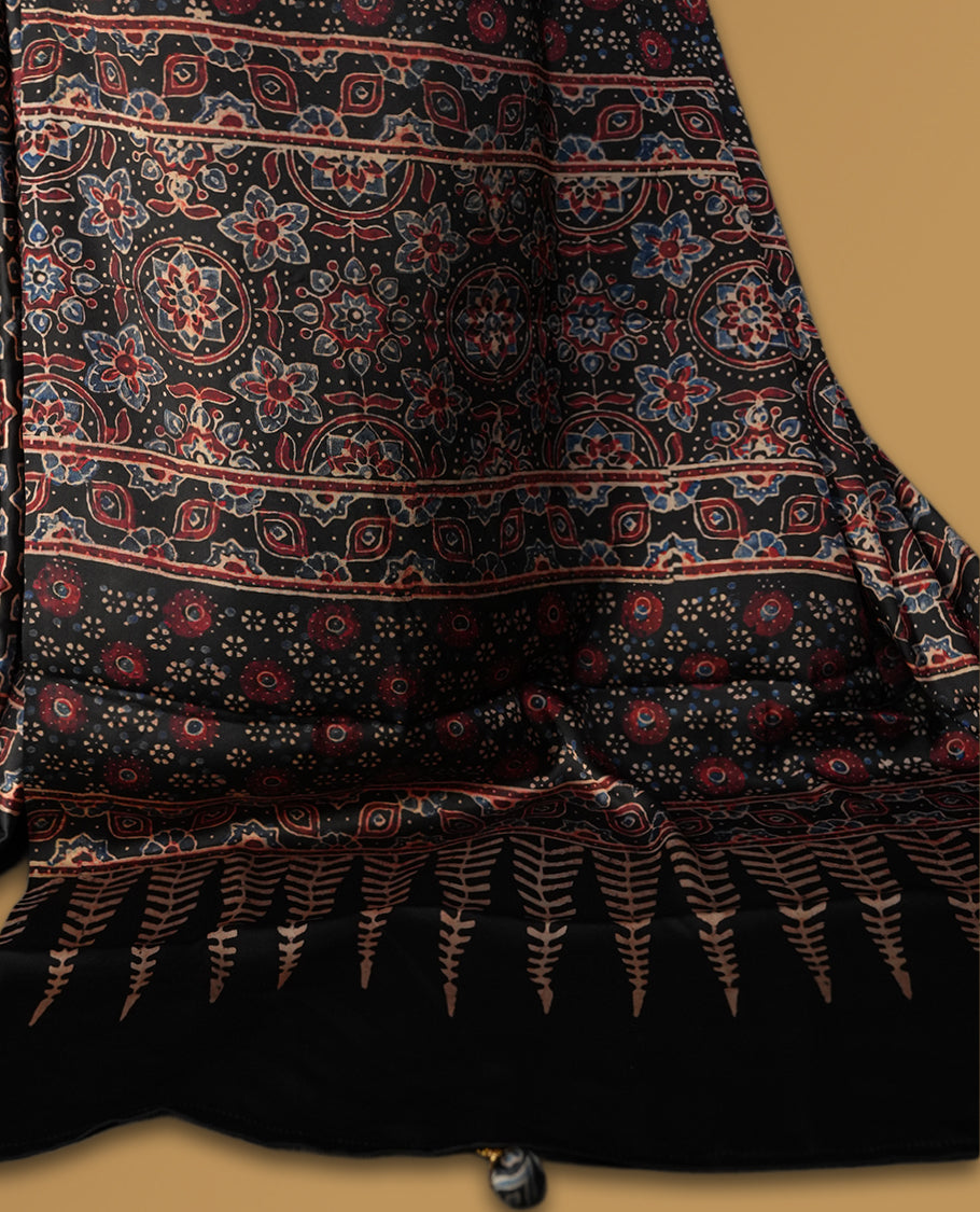Black colour saree featuring intricate traditional prints in earthy tones, finished with a sleek satin border and tassel details & Comes with a stylish matching blouse.