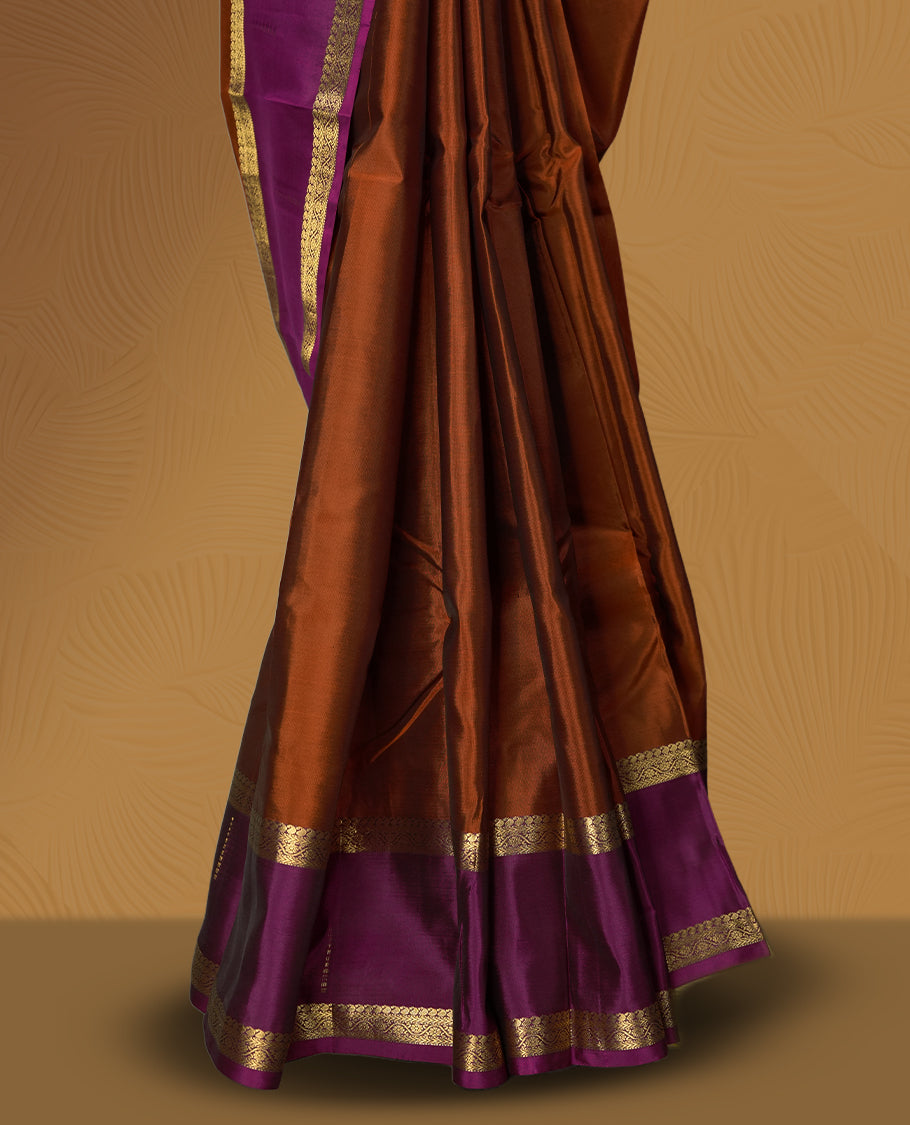 Brown colour soft silk saree adorned with golden zari motifs, complemented by a rich purple border and pallu & Paired with a matching blouse.