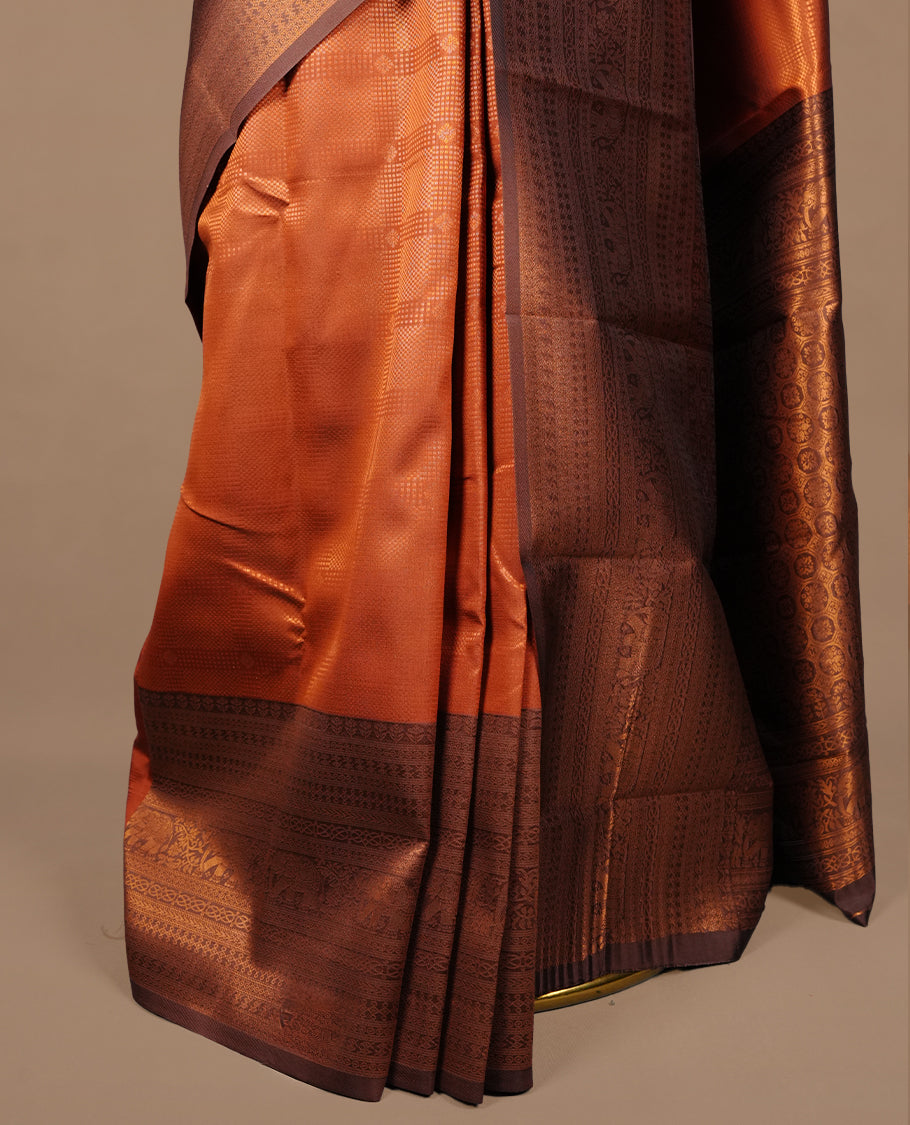 Burnt orange colour silk saree featuring gold zari check and motifs on body, complemented by contrast chocolate with traditional border, paired with matching blouse piece.