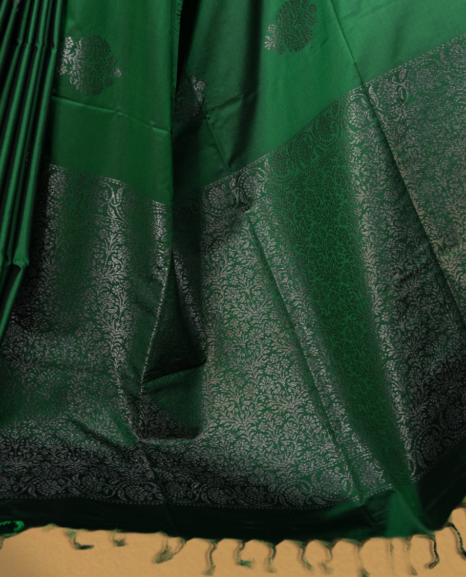 Royal Green colour semi soft silk saree adorned with delicate woven floral motifs on the body, complemented by a rich contrast woven pallu with intricate detailing and tassel accents & Comes with a matching blouse piece.