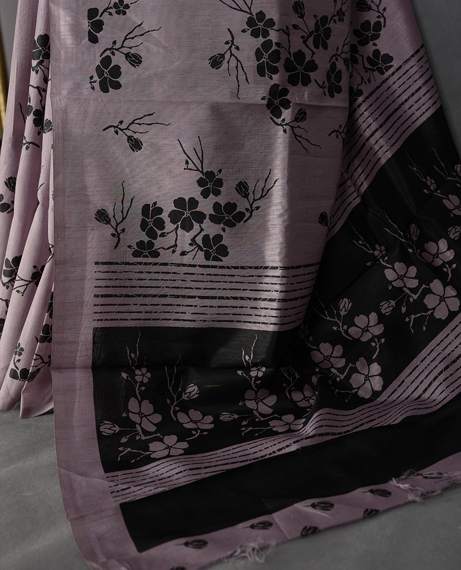 Pastel purple colour saree with delicate black floral prints spread across the body, The black pallu features coordinated floral motifs and stripes, Finished with a sleek border and paired with a matching blouse.