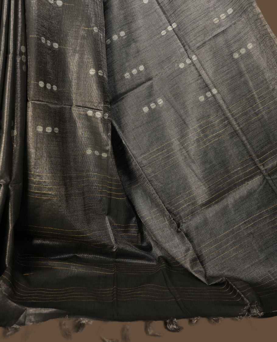 Grey colour semi jute tissue saree accentuated with subtle dotted motifs across the body, The saree features a finely woven pallu and sleek borders, adding a touch of understated elegance & Comes with a matching blouse piece.
