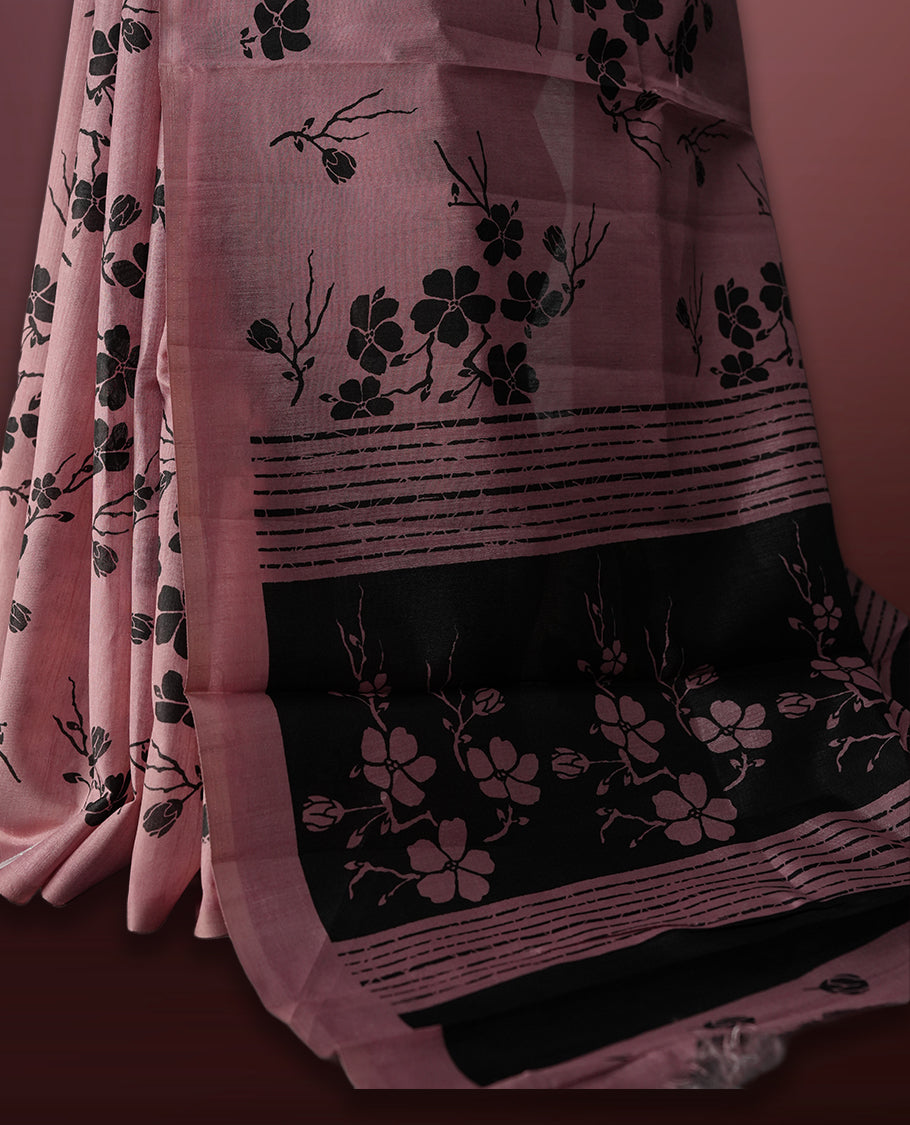 Pastel pink colour saree with black floral prints all over the body, complemented by a contrasting black pallu adorned with bold floral designs and striped detailing & Paired with a matching blouse for a complete look.