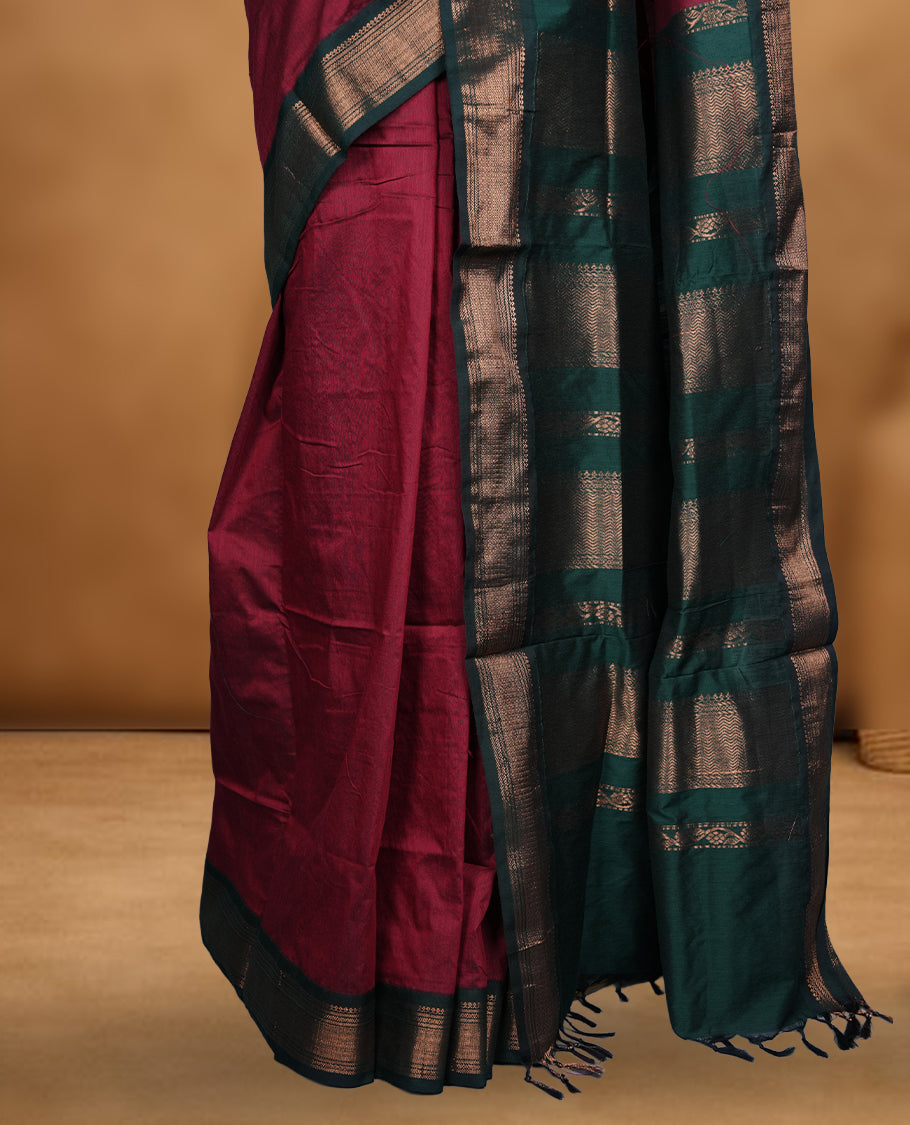 Dark maroon colour Kalyani cotton saree featuring delicate zari buttas on the body, complemented by a dark green zari border and woven pallu, paired with a matching blouse.