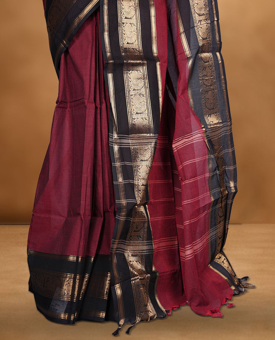 Dark red colour chettinad cotton saree featuring plain body, paired with a black colour traditional gold zari border paired with matching blouse.