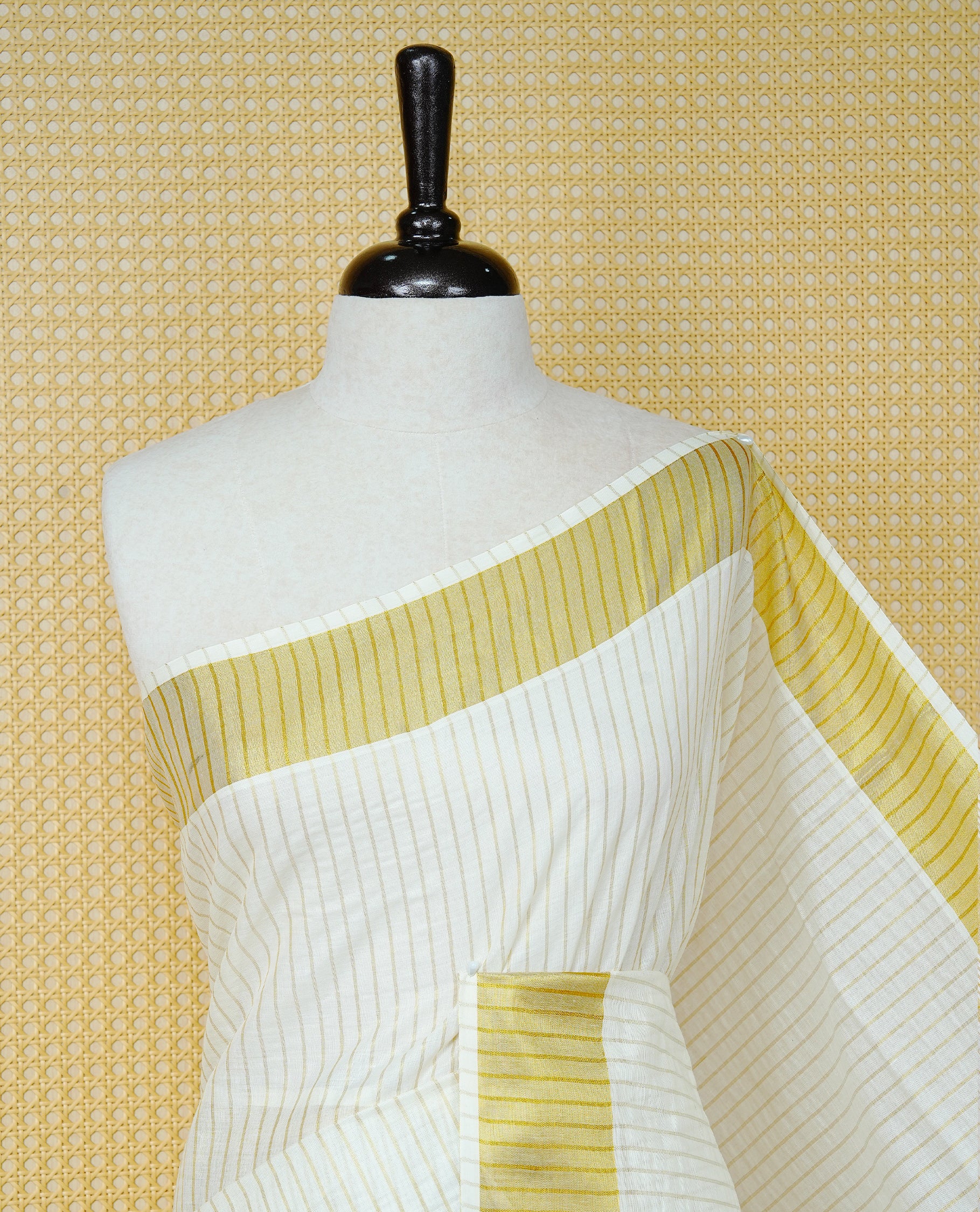 Cream Colur Cotton Kerala Saree Featuring Gold Zari Strips Across On The Body, Classic Gold Zari Border & Pallu,Paired With A Matching Blouse Piece.