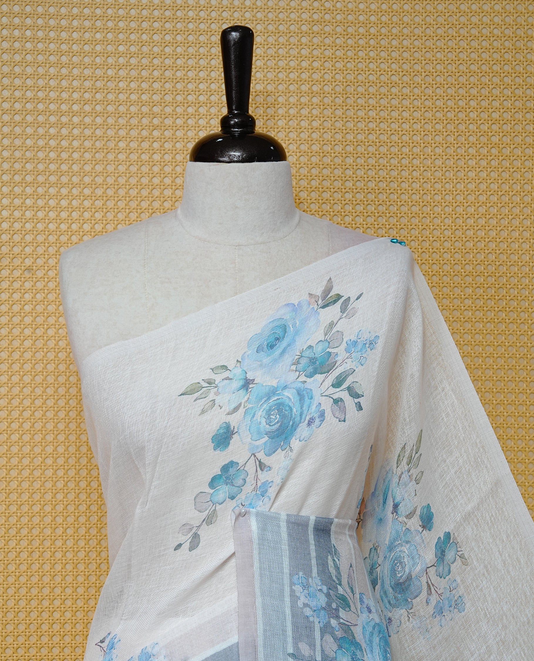 Cream colour semi linen saree featuring Blue colour floral print on body, complemented by contrast Strip pattern border, comes with matching blouse piece.