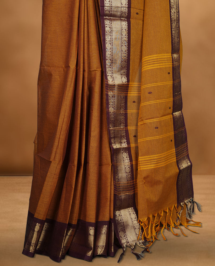 Mustard Brown colour chettinad cotton saree featuring plain body, paired with a black colour traditional gold zari border paired with matching blouse.