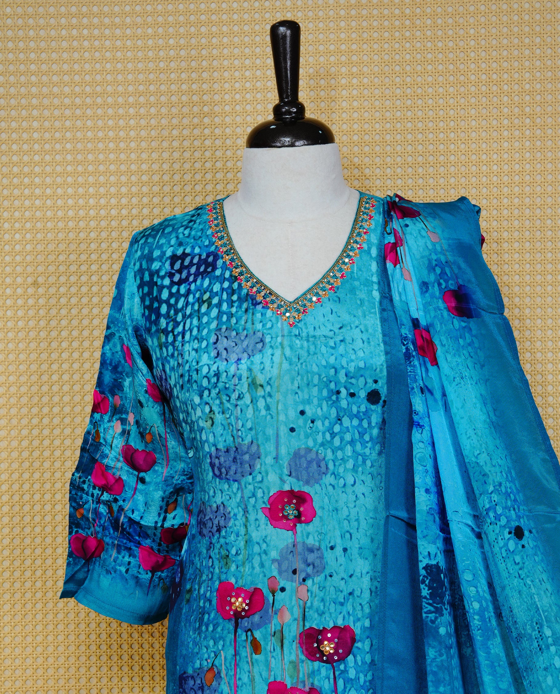 Blue colour churidar set featuring vibrant floral prints and delicate bead work on the V-neckline, paired with matching solid pants and a floral printed dupatta.