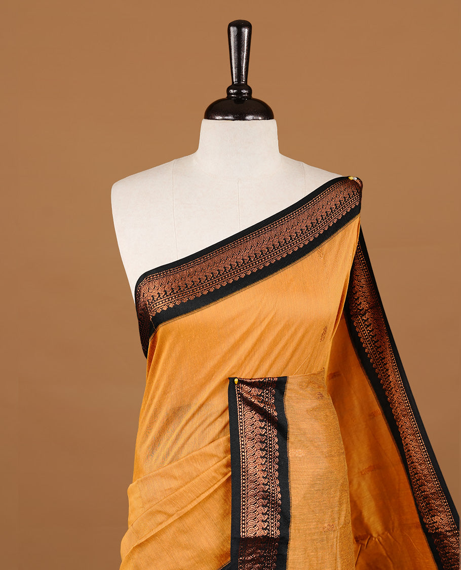 Mustard colour kalyani cotton saree featuring gold zari motifs on body, highlighting contrast Black colour with Antique gold zari border, paired with matching blouse piece.