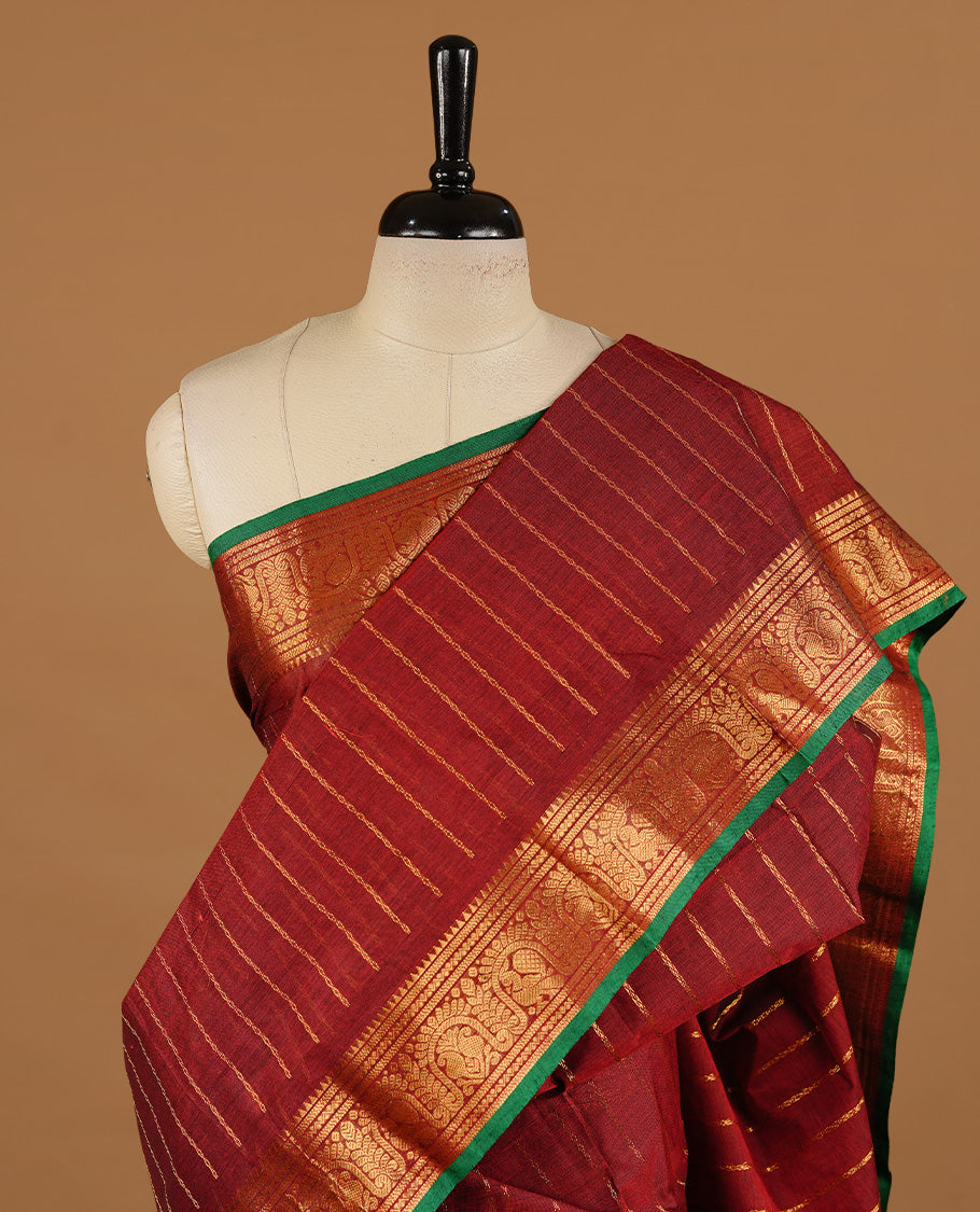 Maroon colour chettinad cotton saree featuring gold zari stripes on body, complemented by self colour with zari green colour piping border, paired with matching blouse piece.