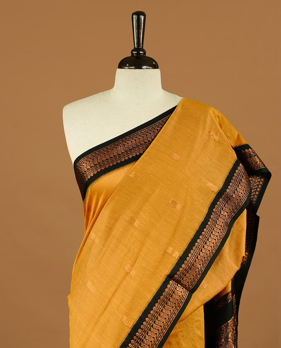 Mustard colour kalyani cotton saree featuring gold zari motifs on body, highlighting contrast Black colour with Antique gold zari border, paired with matching blouse piece.