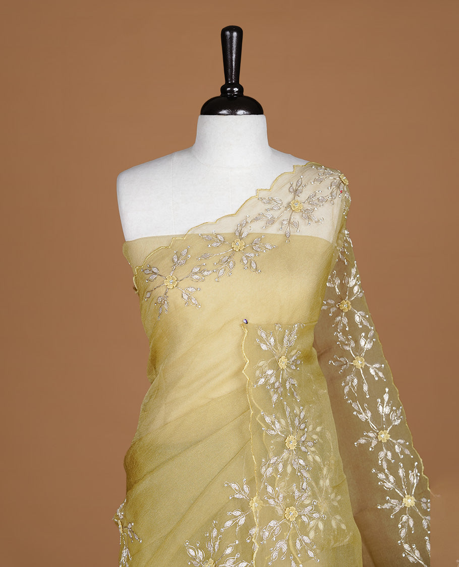 Pastel olive colour crush organza saree featuring gold thread floral and stone worked body, highlighting scalp designed border, paired with matching blouse piece.