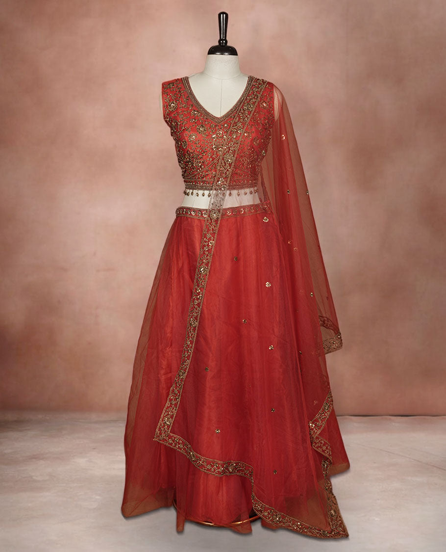 Red colour lehenga set with stitched sleeveless Antique thread embroidered & beats worked blouse featuring sheer neckline, matching stitched flared lehenga, and plain sheer dupatta.