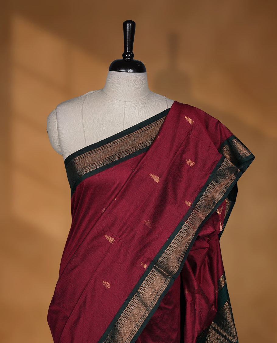 Dark maroon colour Kalyani cotton saree featuring delicate zari buttas on the body, complemented by a dark green zari border and woven pallu, paired with a matching blouse.