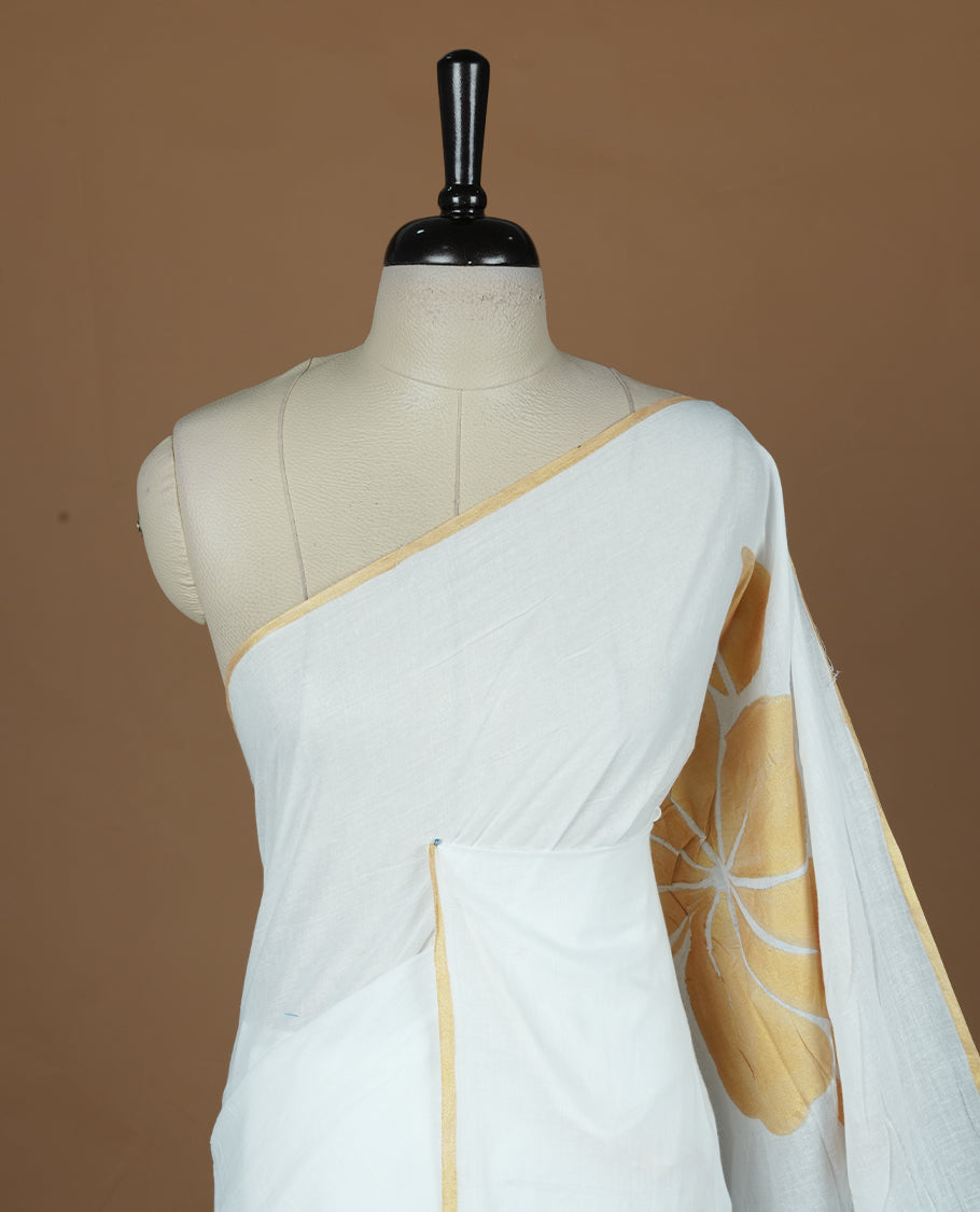 White coloured mul cotton saree featuring bold gold-tone floral motifs across the body, designed without a border and comes without a blouse piece.
