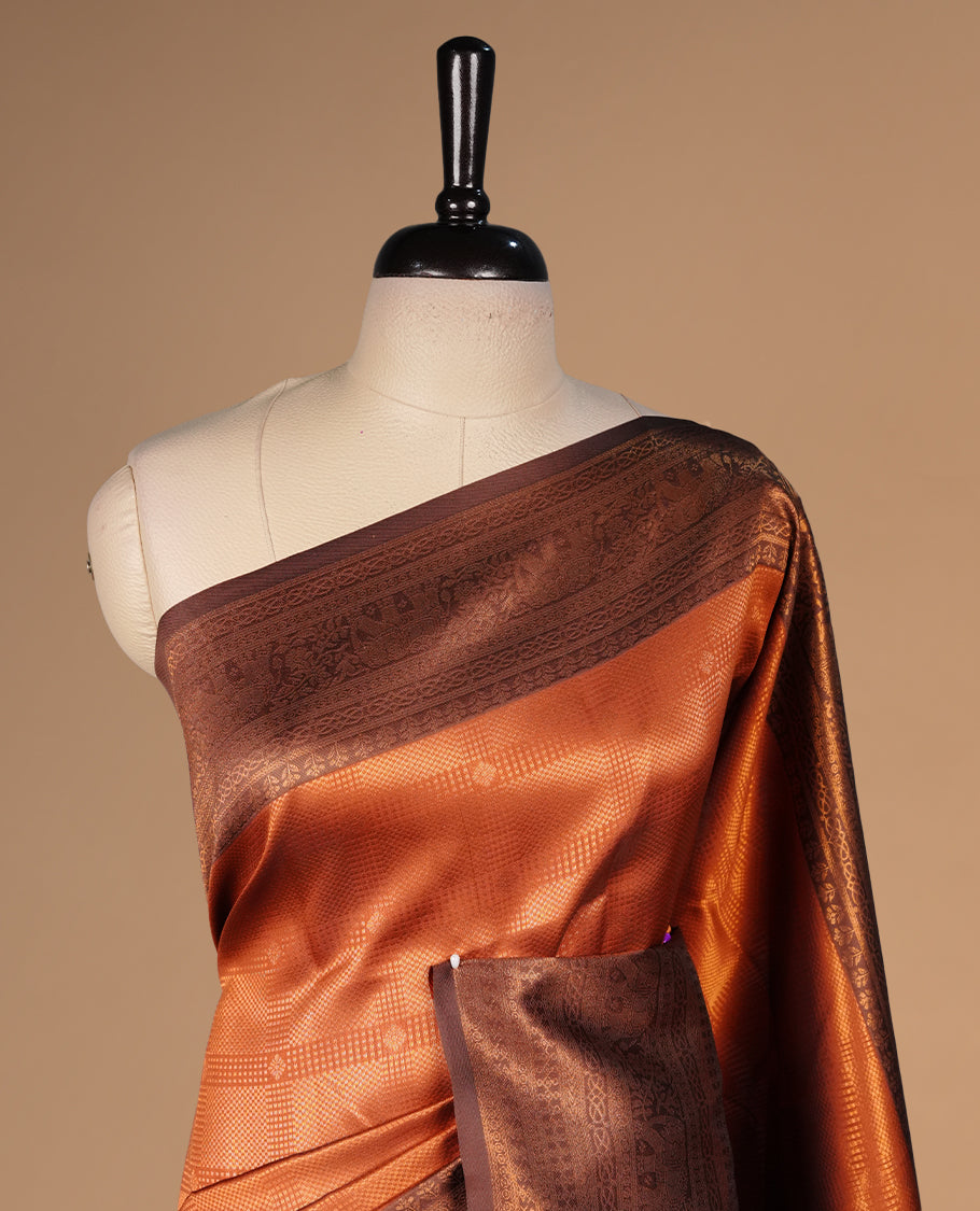 Burnt orange colour silk saree featuring gold zari check and motifs on body, complemented by contrast chocolate with traditional border, paired with matching blouse piece.