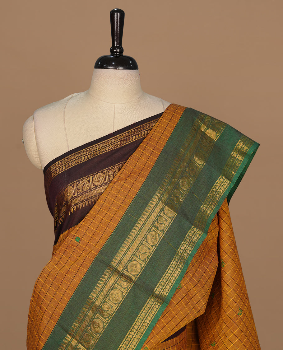 Mustard colour chettinad cotton featuring check pattern on body, complemented by contrast chocolate brown colour with gold zari border, paired with matching blouse piece.