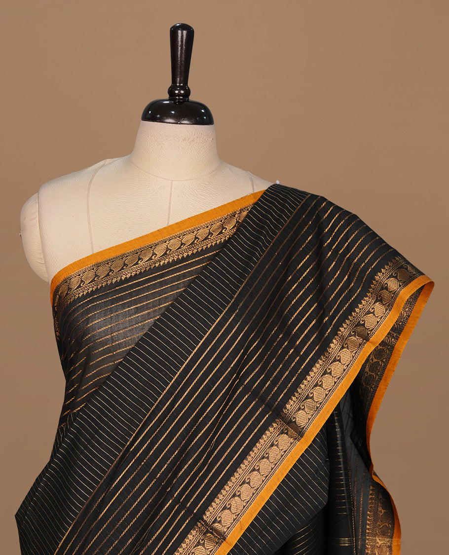 Black colour chettinad cotton saree featuring gold zari stripes on body, complemented by yellow piping with gold zari border, paired with matching blouse piece.