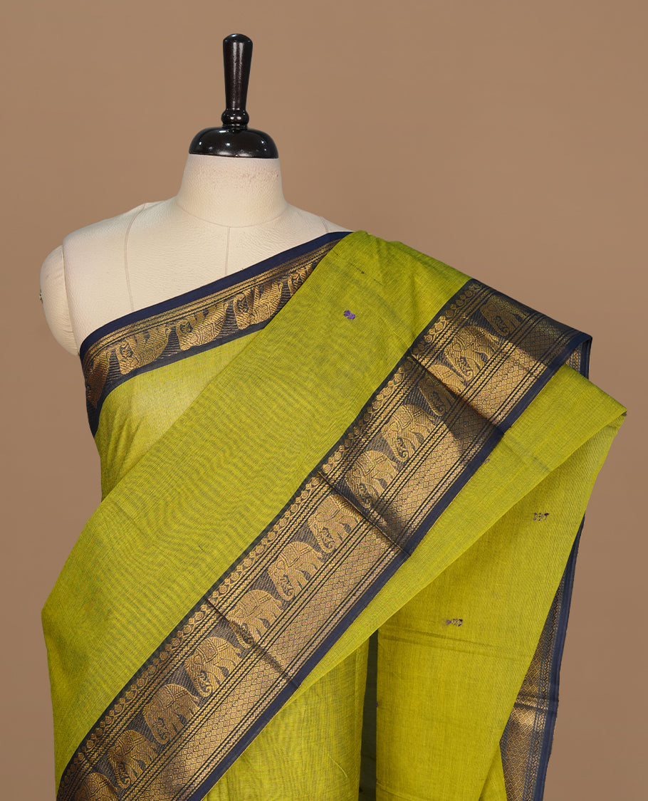 Olive green colour chettinad cotton saree featuring small buttas on body, complemented by contrast blue colour with gold zari border, paired with matching blouse piece.
