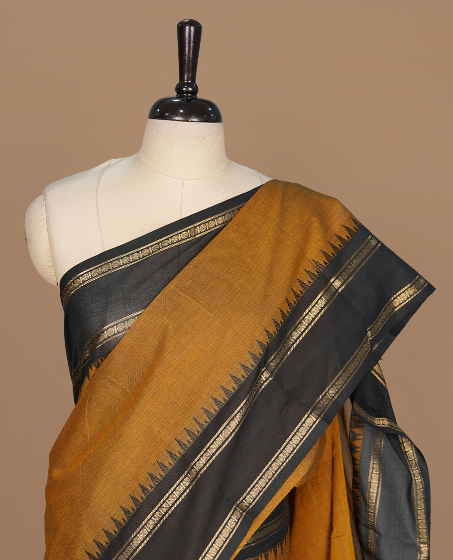 Bronze colour chettinad cotton saree featuring elegant plain body, complemented by contrast black with gold zari border, paired with matching blouse piece.