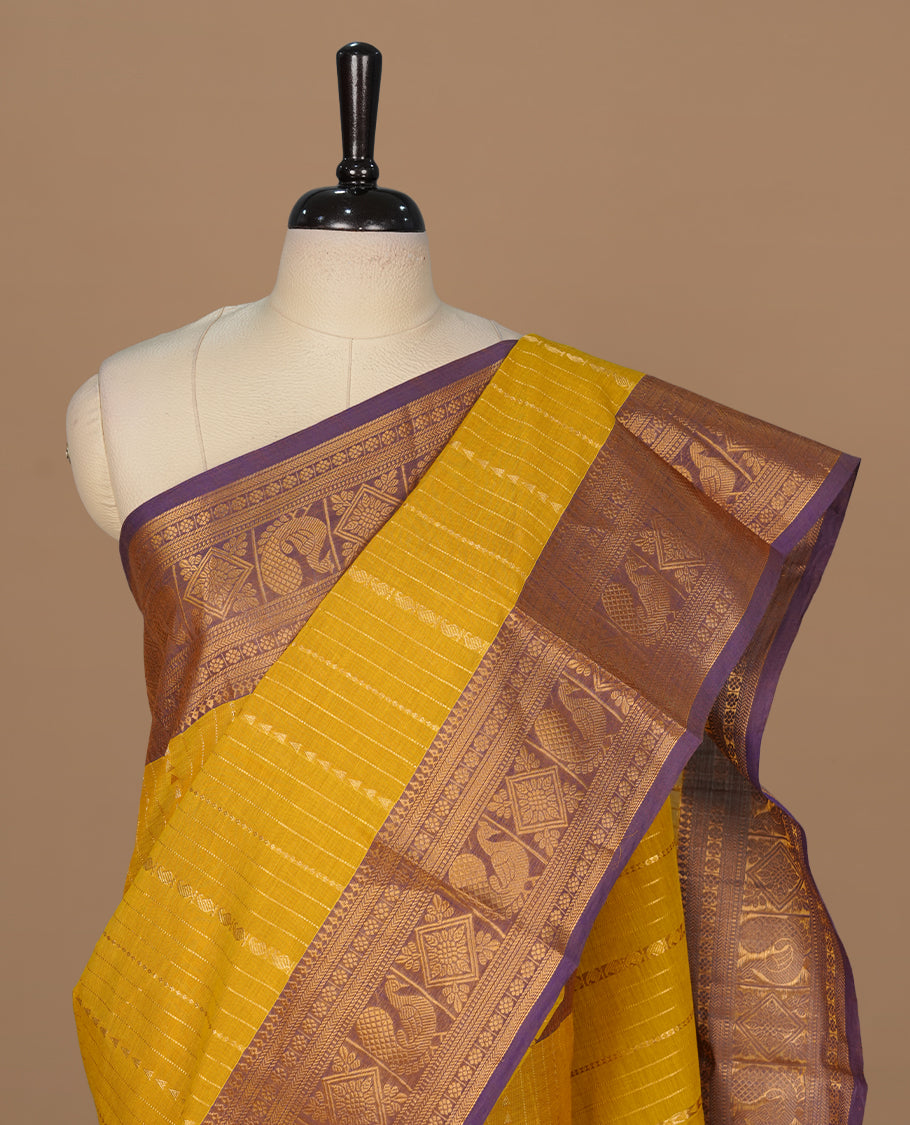 Olive yellow colour chettinad saree featuring gold zari motifs on body, complemented by contrast purple colour with traditional border, paired with matching blouse piece.