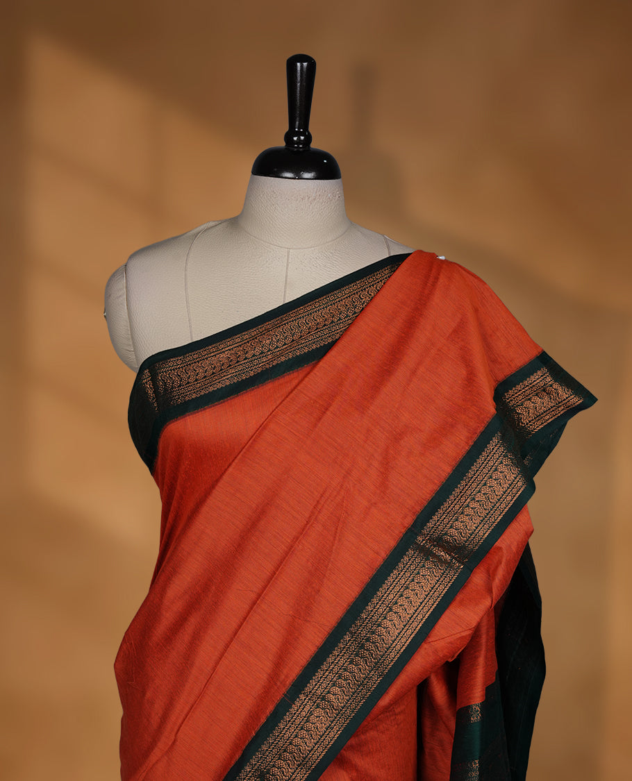 Rust orange colour Kalyani cotton saree featuring a plain elegant body, complemented by a rich green zari border and traditional woven pallu, paired with a matching blouse.