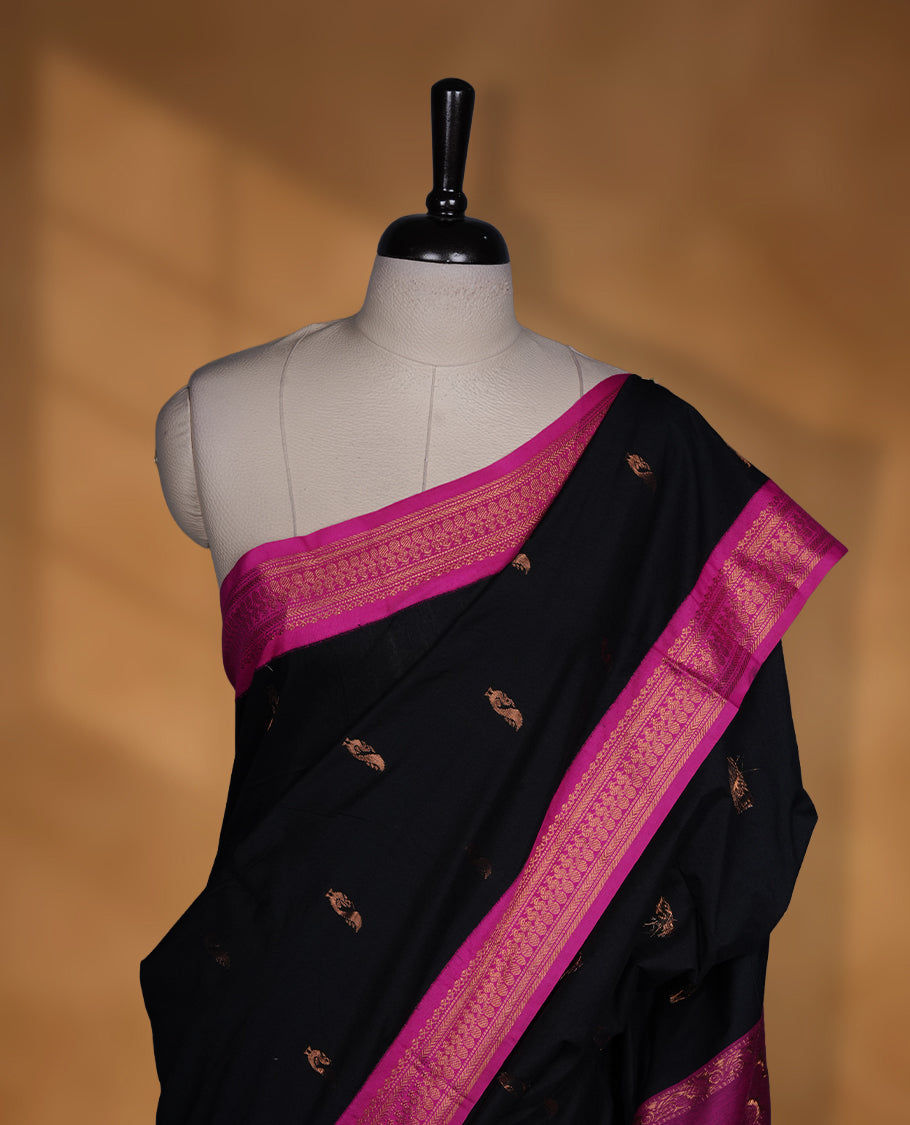Black colour Kalyani cotton saree featuring delicate zari buttas on the body, complemented by a magenta zari border and woven pallu, paired with a matching blouse.