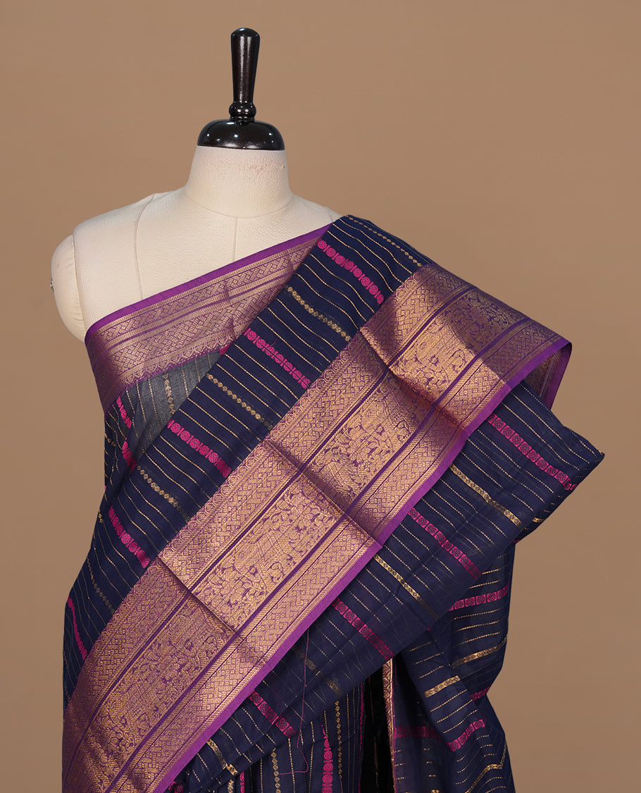Navy blue colour chettinad saree featuring gold zari stripes on body, complemented by contrast Purple colour with traditional border, paired with matching blouse piece.