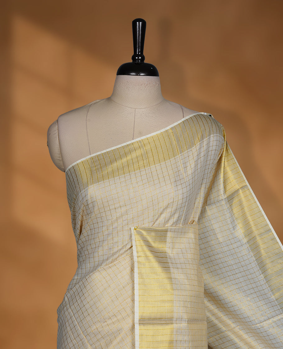 Off white colour Tissue Kerala saree featuring a subtle checked body, a refined golden zari border, and a traditionally woven pallu, paired with a matching blouse.