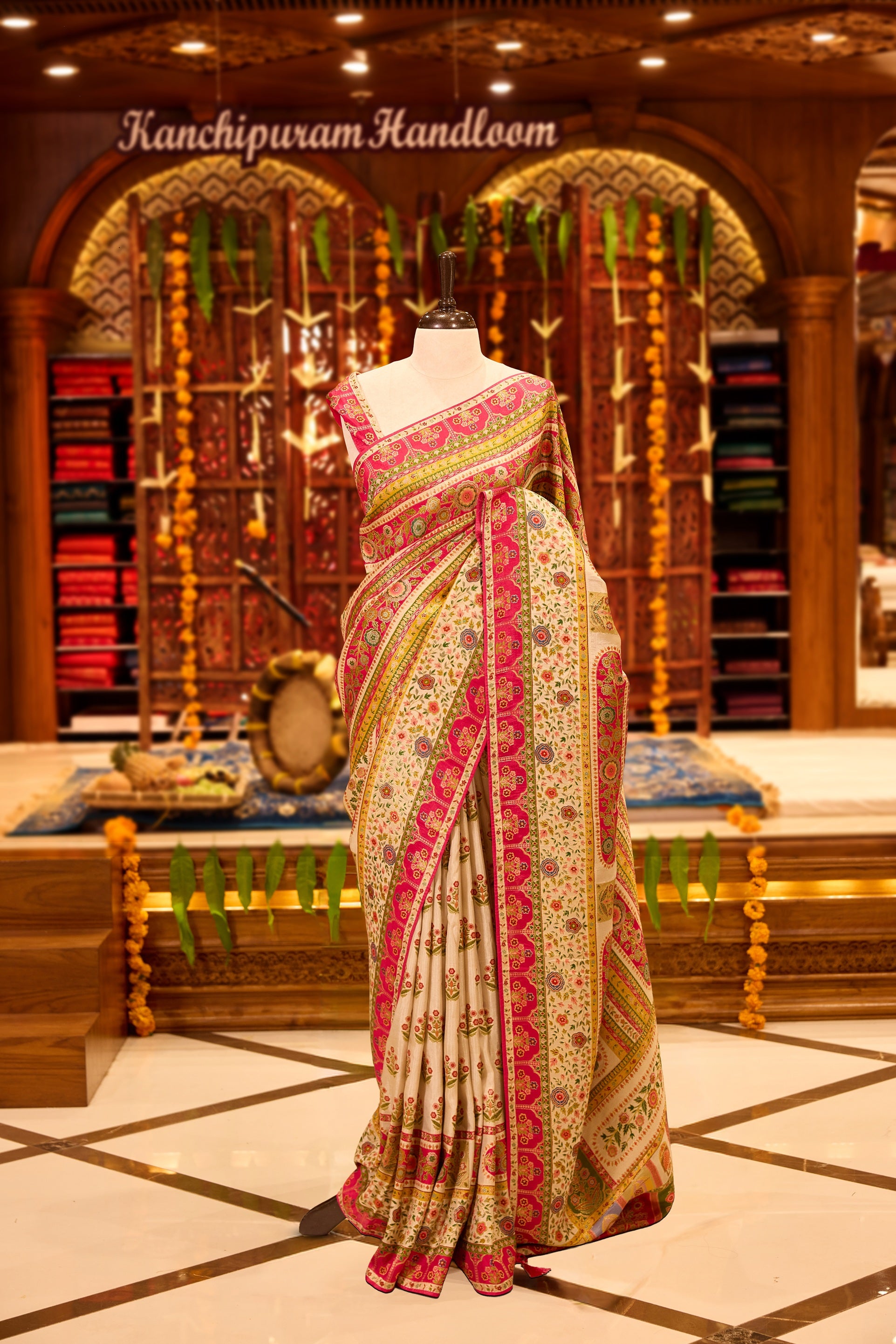 Ivory colour Pashmina silk saree richly adorned with intricate multicolour floral motifs across the body, accentuated by vibrant pink and green ornamental borders and a grand storytelling pallu, beautifully paired with a matching blouse piece.