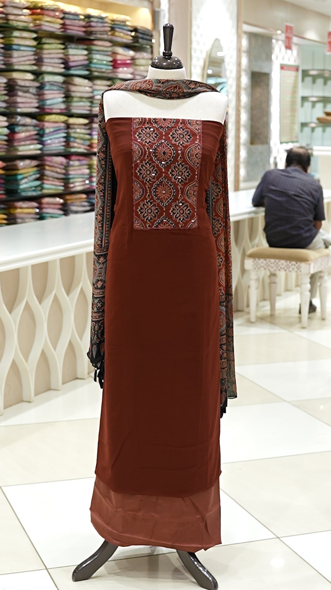 Brick red Georgette salwar material featuring Ajrakh print with mirror work on the yoke, paired with Ajrakh printed dupatta with mirror detailing and plain bottom.