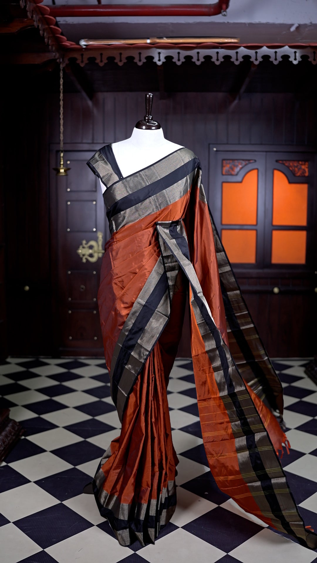 Burnt Orange colour Arani Silk saree featuring a plain body with elegant contrast Black borders, comes with a matching blouse piece.