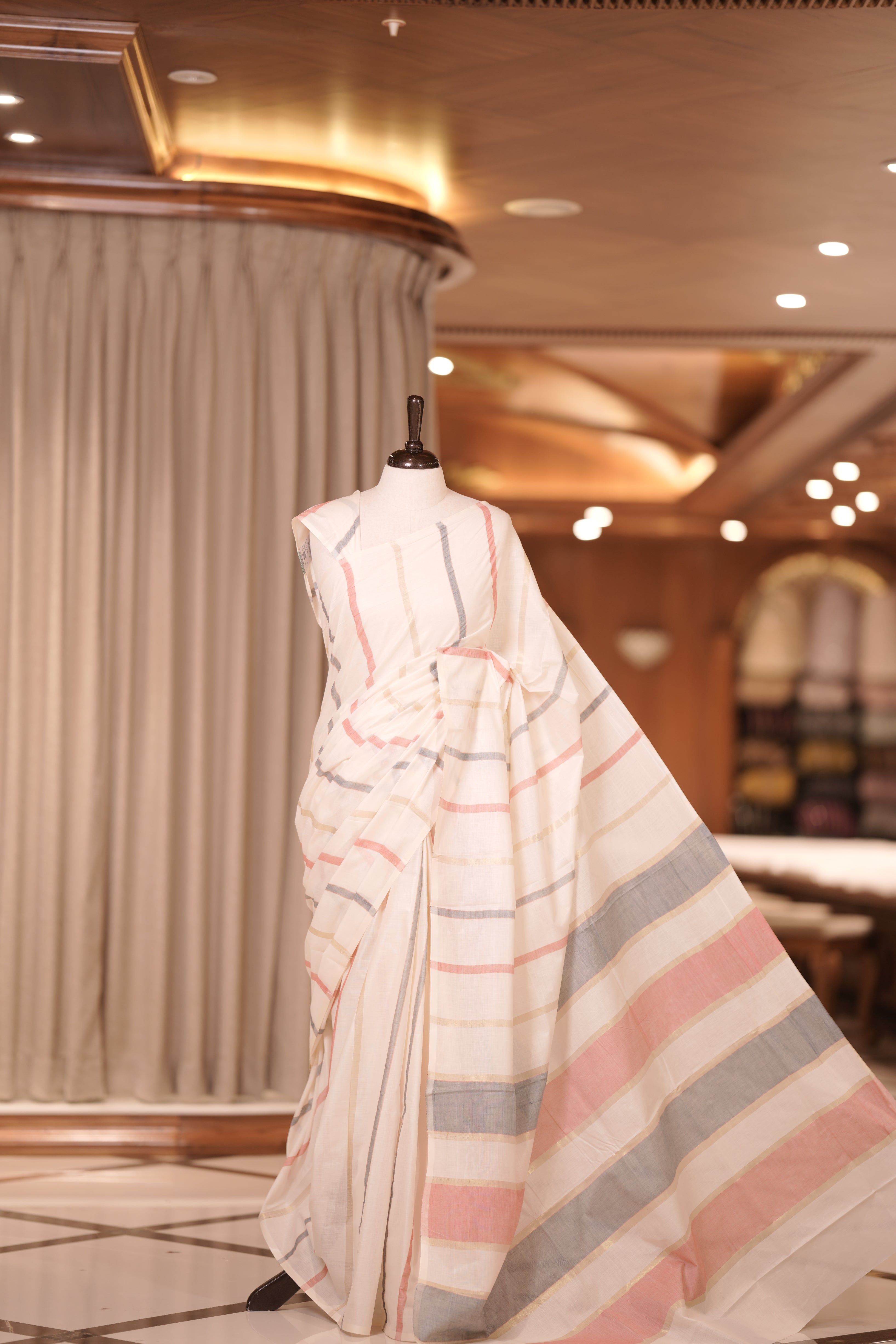 Cream colour handloom cotton saree adorned with light golden lines and a subtle coral red shade & The matching pallu enhances its timeless charm, making it perfect for graceful traditional and festive occasions.