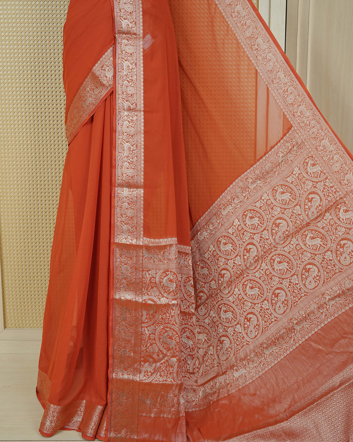 Rust orange colour georgette saree having plain body, peacock & deer gold zari detailed border, comes with matching blouse piece