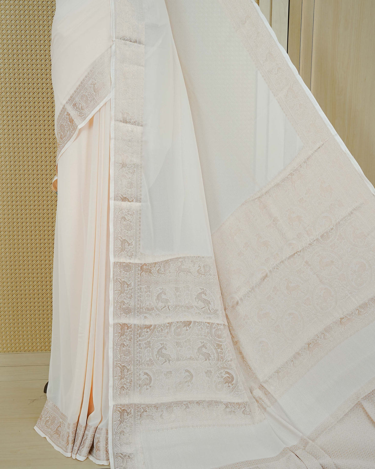Cream colour georgette saree having plain body, peacock & deer gold zari detailed border, comes with matching blouse piece