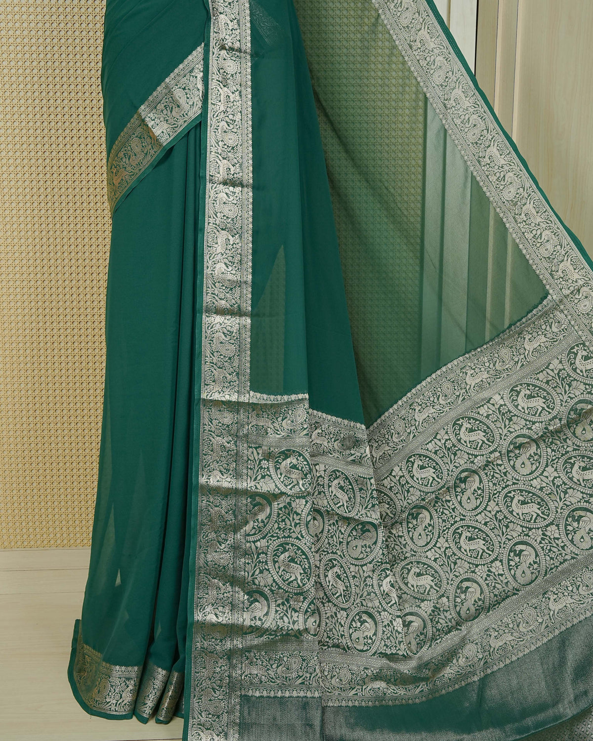 Bottle green colour georgette saree having plain body, peacock & deer gold zari detailed border, comes with matching blouse piece