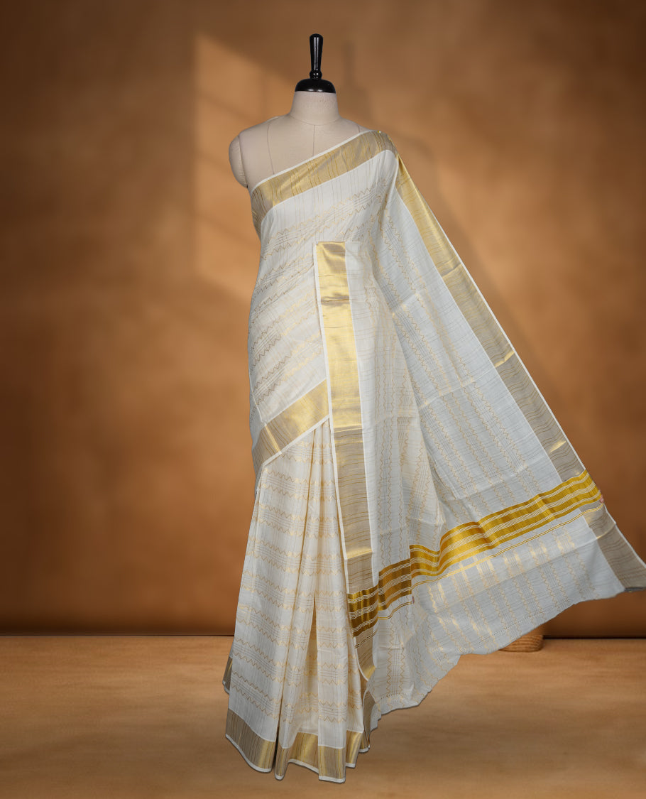 Off white Cotton Kerala saree featuring a subtle zari patterned body, complemented by a classic golden zari border and traditional pallu, paired with a matching blouse.