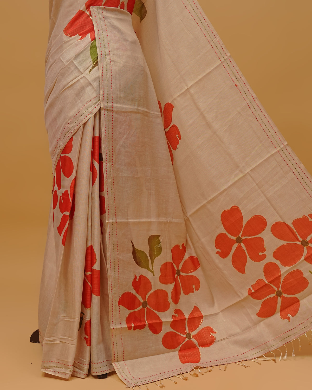 Cream colour Semi Tissue saree featuring Red colour Floral Motifs on body, a Threaded border & pallu,finished with tassels, paired with a matching blouse piece.
