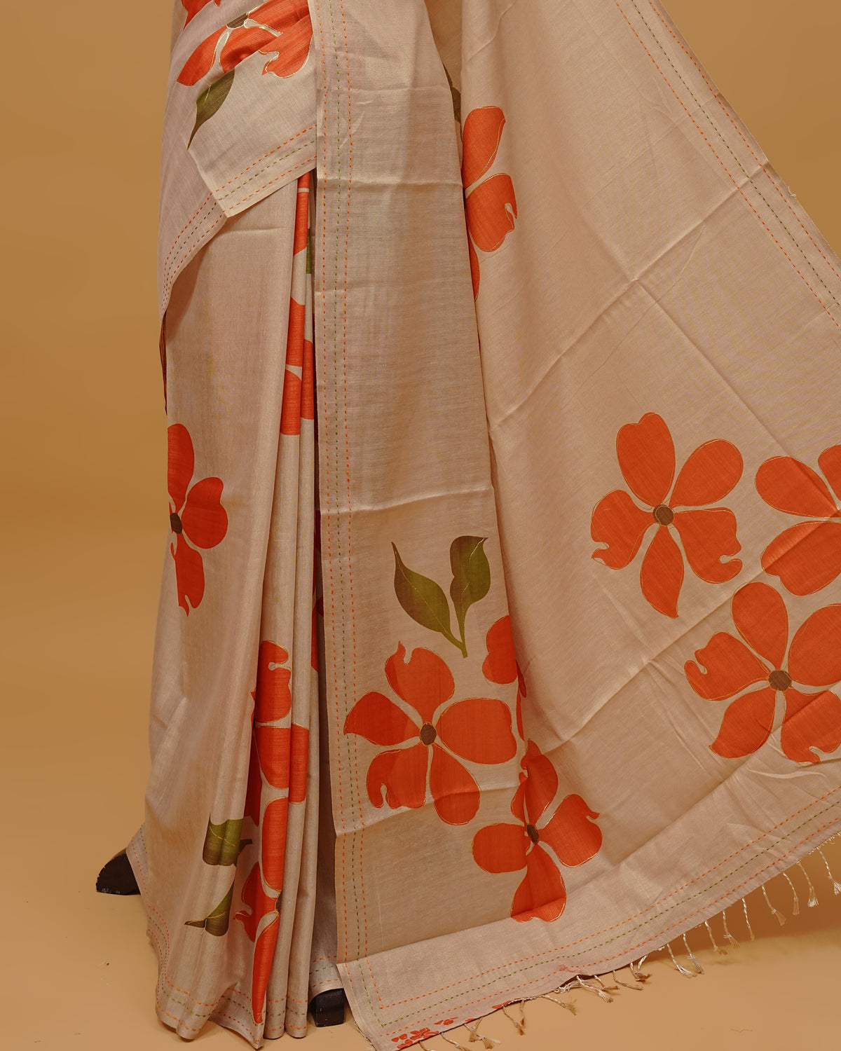Cream colour Semi Tissue saree featuring Orange Colour Floral Motifs Design on the body, a Threaded border & a pallu finished with tassels, paired with a matching blouse piece.