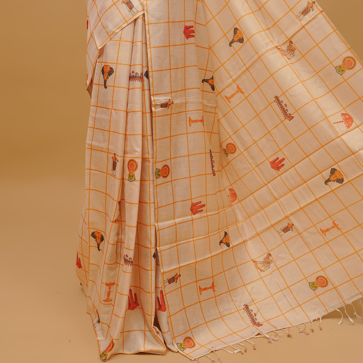 Cream colour semi tissue saree featuring traditional Kerala festival prints in checked body, without a border & pallu finished with tassels. Paired with a matching blouse piece.