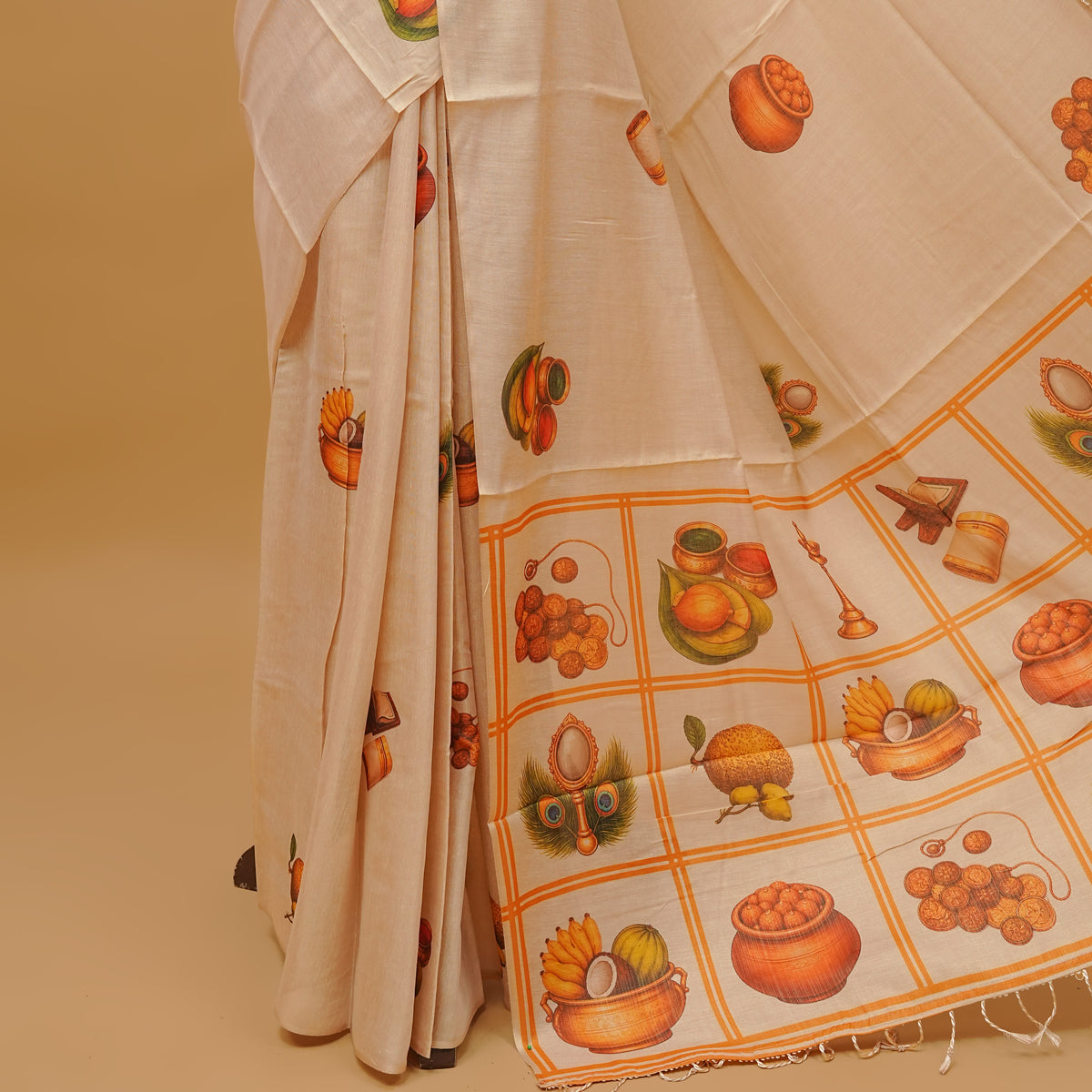 Cream colour semi tissue saree featuring Vishu theme prints on the body, without border & pallu finished with tassels. Paired with a matching blouse piece.