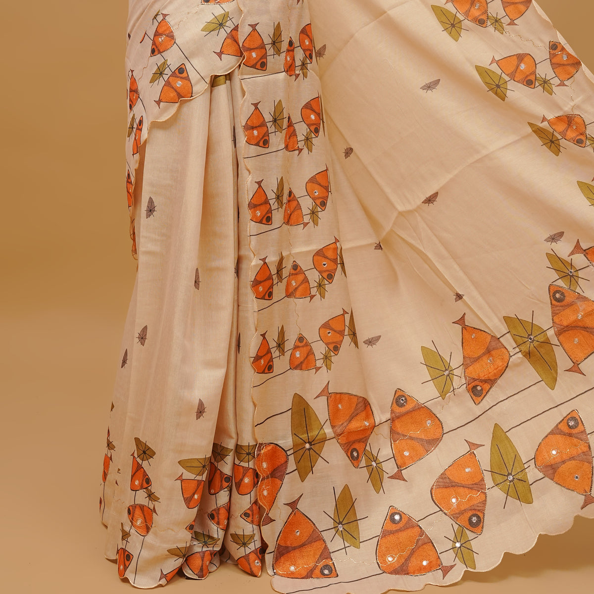 Cream colour semi tissue saree featuring fish prints with Mirror Work on the body, with scallop border & pallu finished with tassels. Paired with a matching blouse piece.