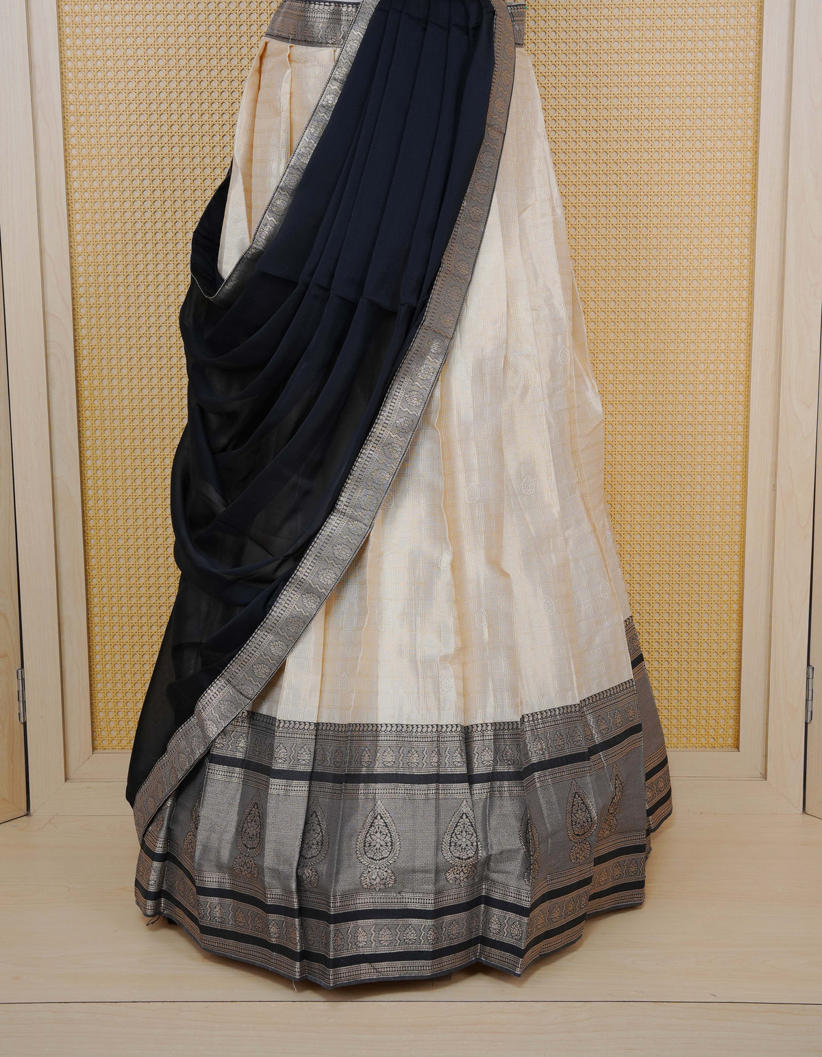 Cream colour Semi Silk Semi stitched dhavani set featuring Gold zari check pattern with motifs on body ,contrast Black colour with gold zari bordered skirt, paired with matching blouse piece & dupatta.