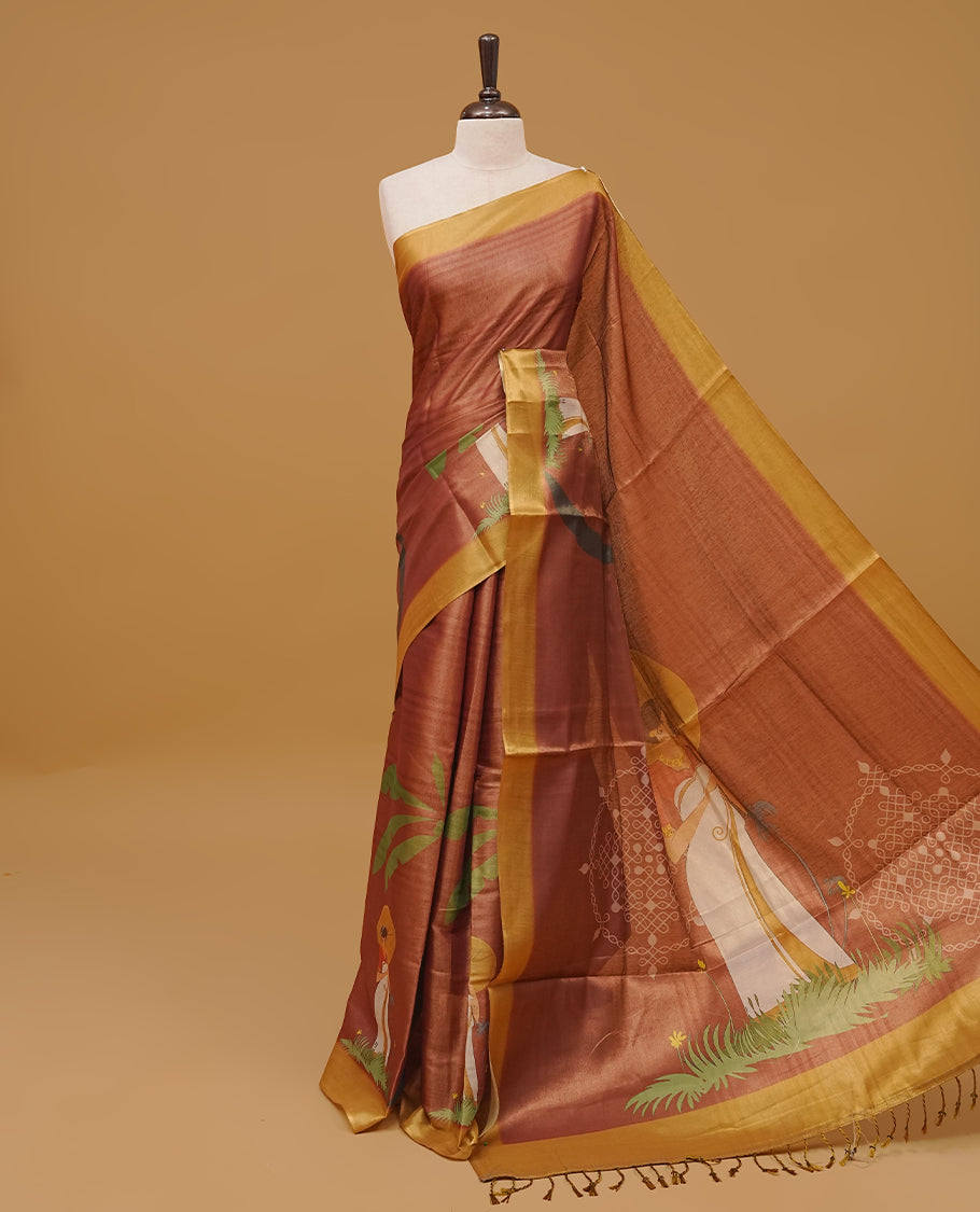 Brown colour semi tissue saree featuring a lady prints on body, with a Gold colour border & pallu finished with tassels. Paired with a matching blouse piece.