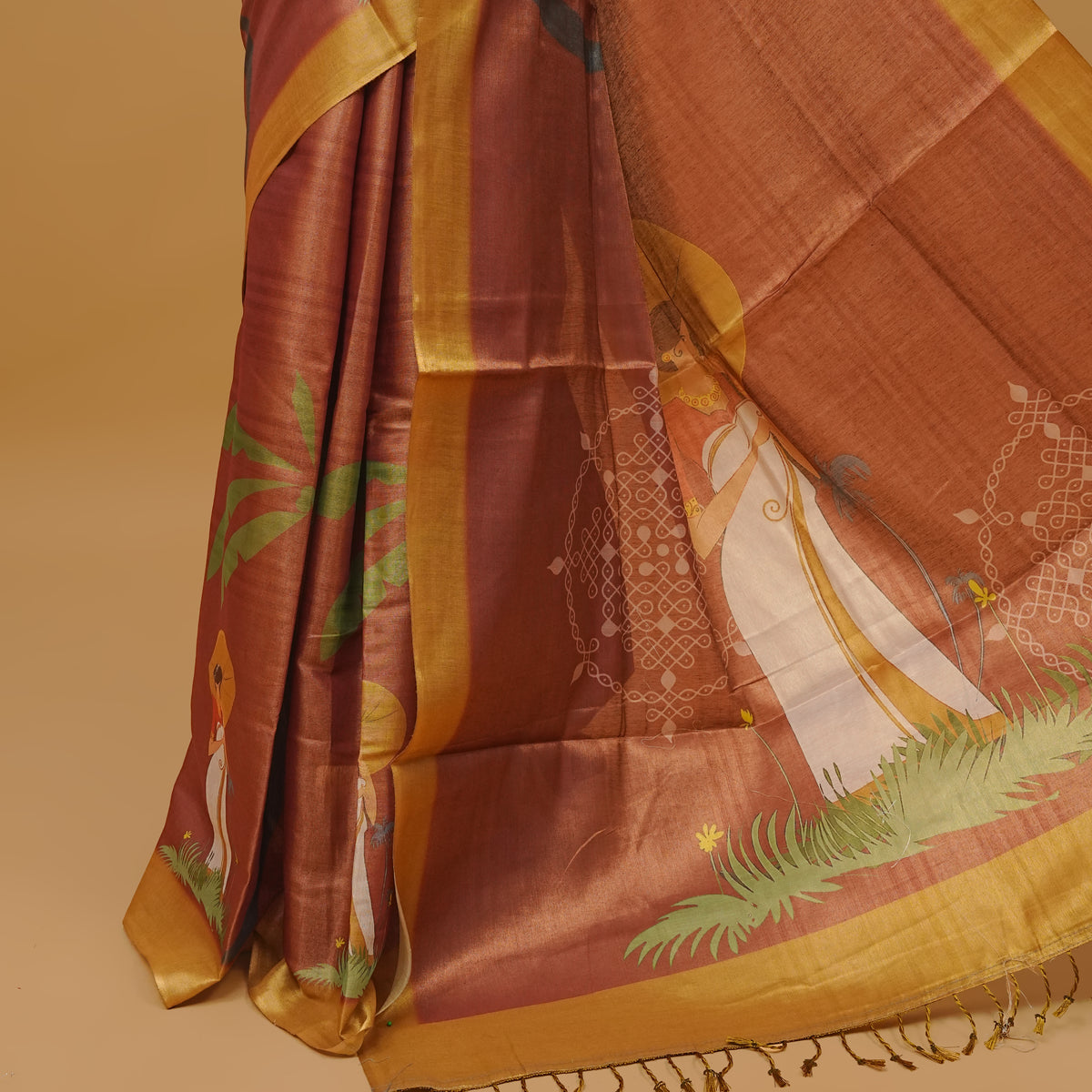 Brown colour semi tissue saree featuring a lady prints on body, with a Gold colour border & pallu finished with tassels. Paired with a matching blouse piece.