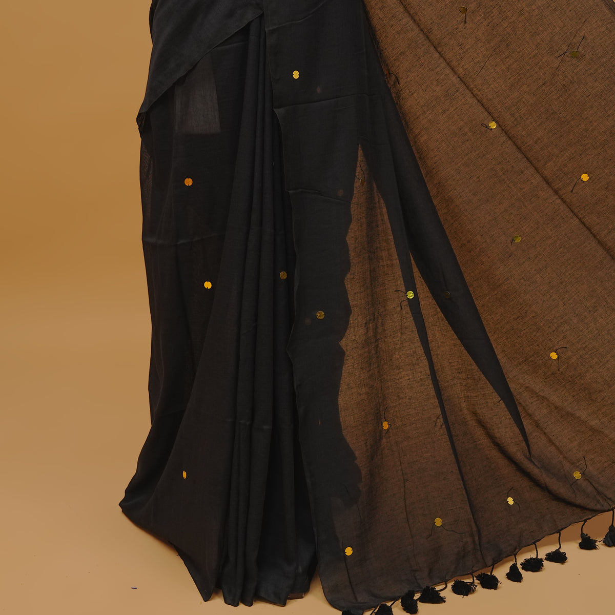 Black colour mul cotton saree featuring sequin work on body, without a border & pallu finished with tassels. Paired with a matching blouse piece.