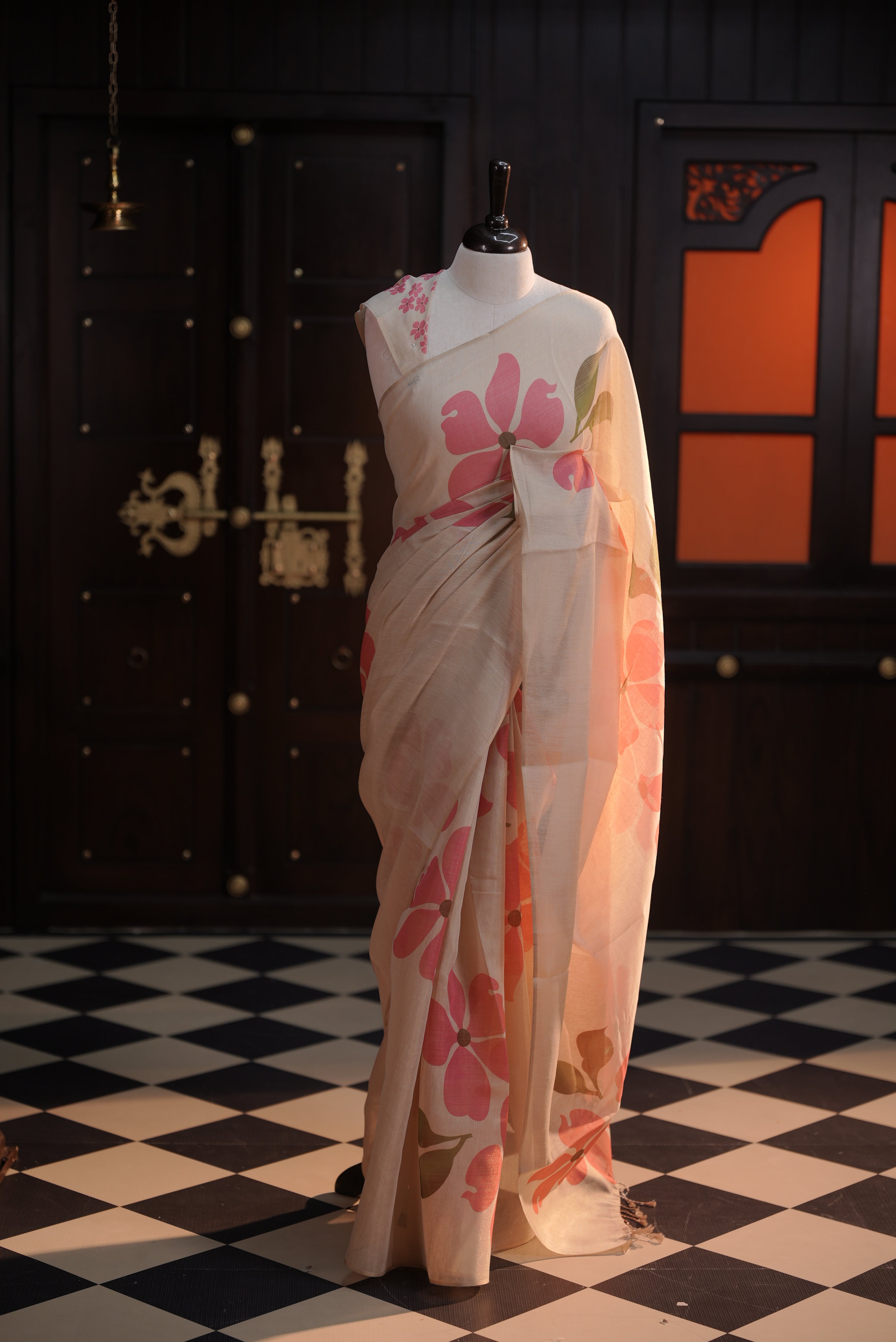 Beige colour semi soft tissue saree adorned with bold Pink floral prints across the body, designed without a border, paired with a matching blouse piece featuring delicate flower motifs.