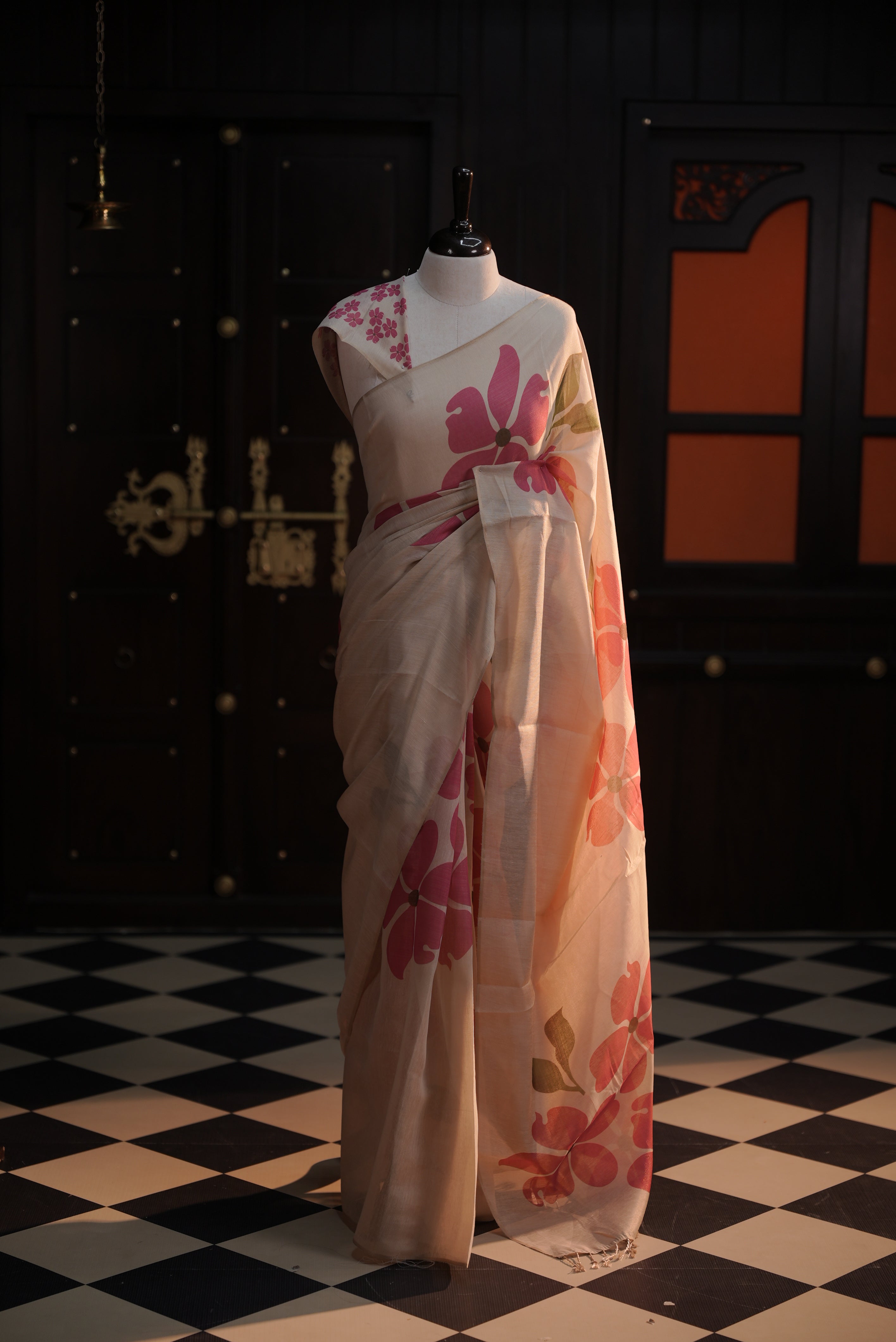 Beige colour semi soft tissue saree adorned with bold magenta floral prints across the body, designed without a border, paired with a matching blouse piece featuring delicate flower motifs.